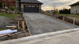 New driveway with compacted gravel, wooden stakes, and string lines leading to a residential garage.